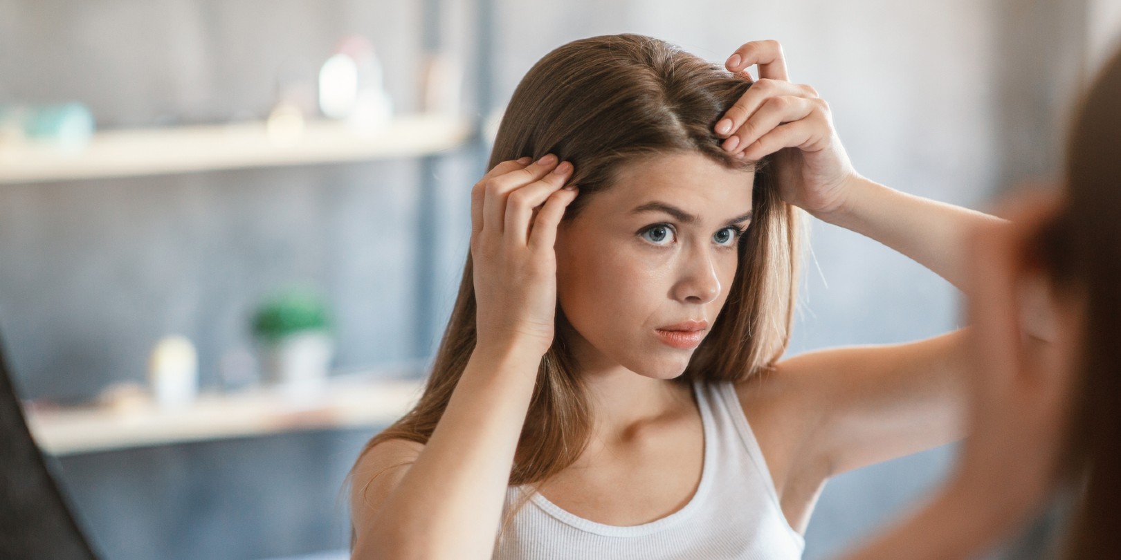 Millennial girl with hair dandruff problem looking in mirror at home