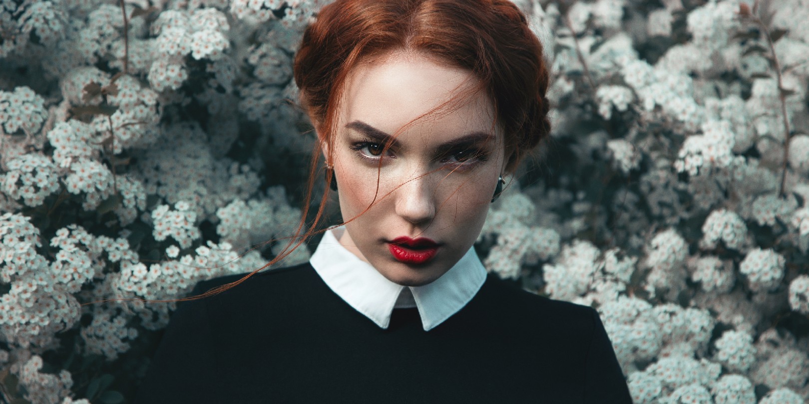 Pretty girl with curly redhair in the park with flowers on background