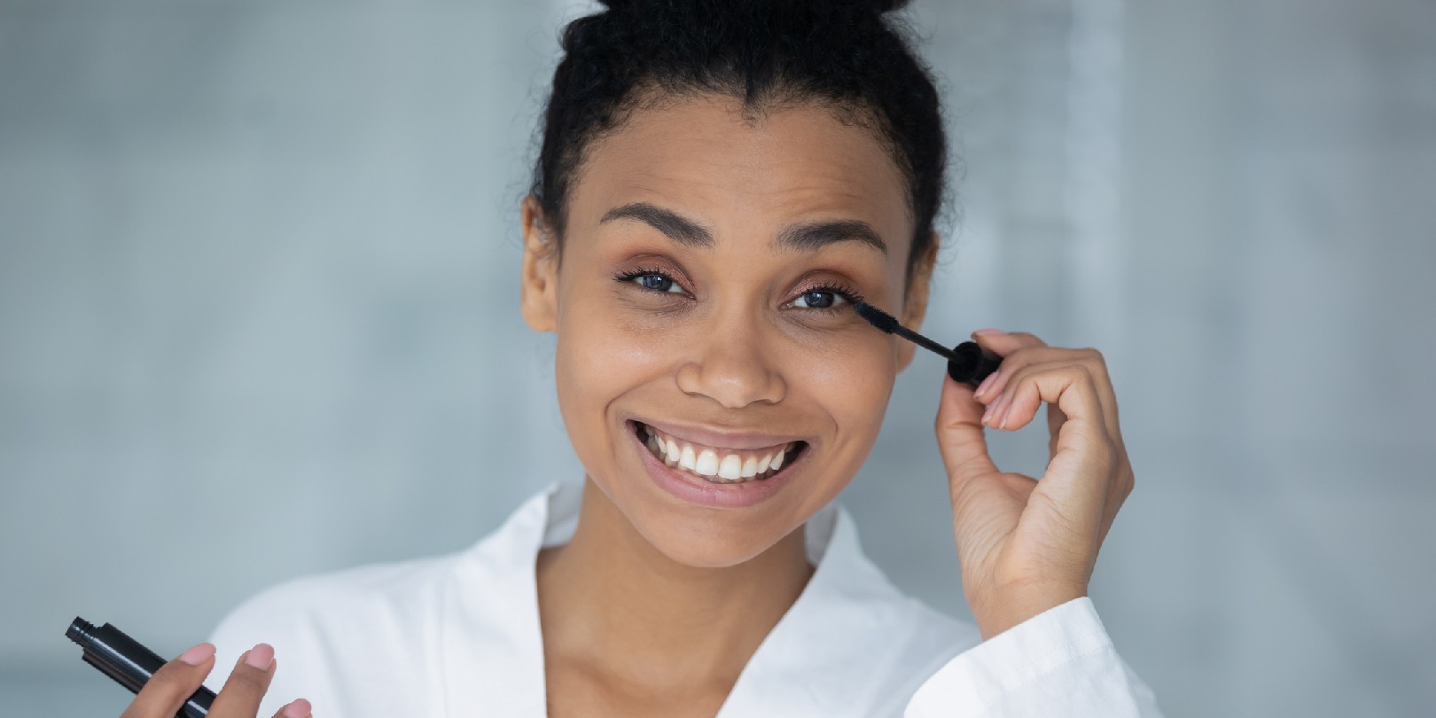 Head shot portrait african woman holding black tube applying volumizing mascara
