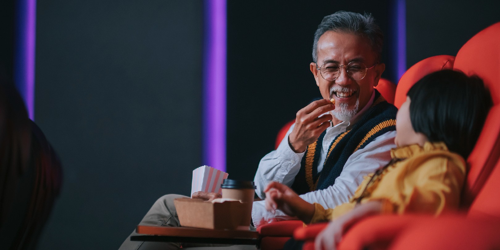 style-a-sweater-vest the-independence Asian chinese active senior man and his granddaughter enjoy watching movie in cinema movie theatre