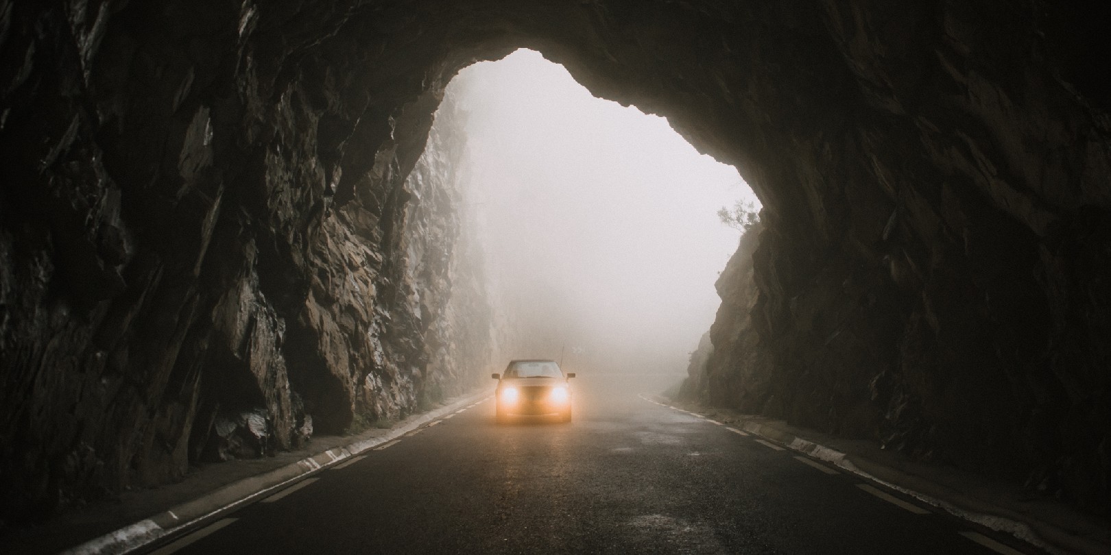 A car with lights on, entering a tunnel road