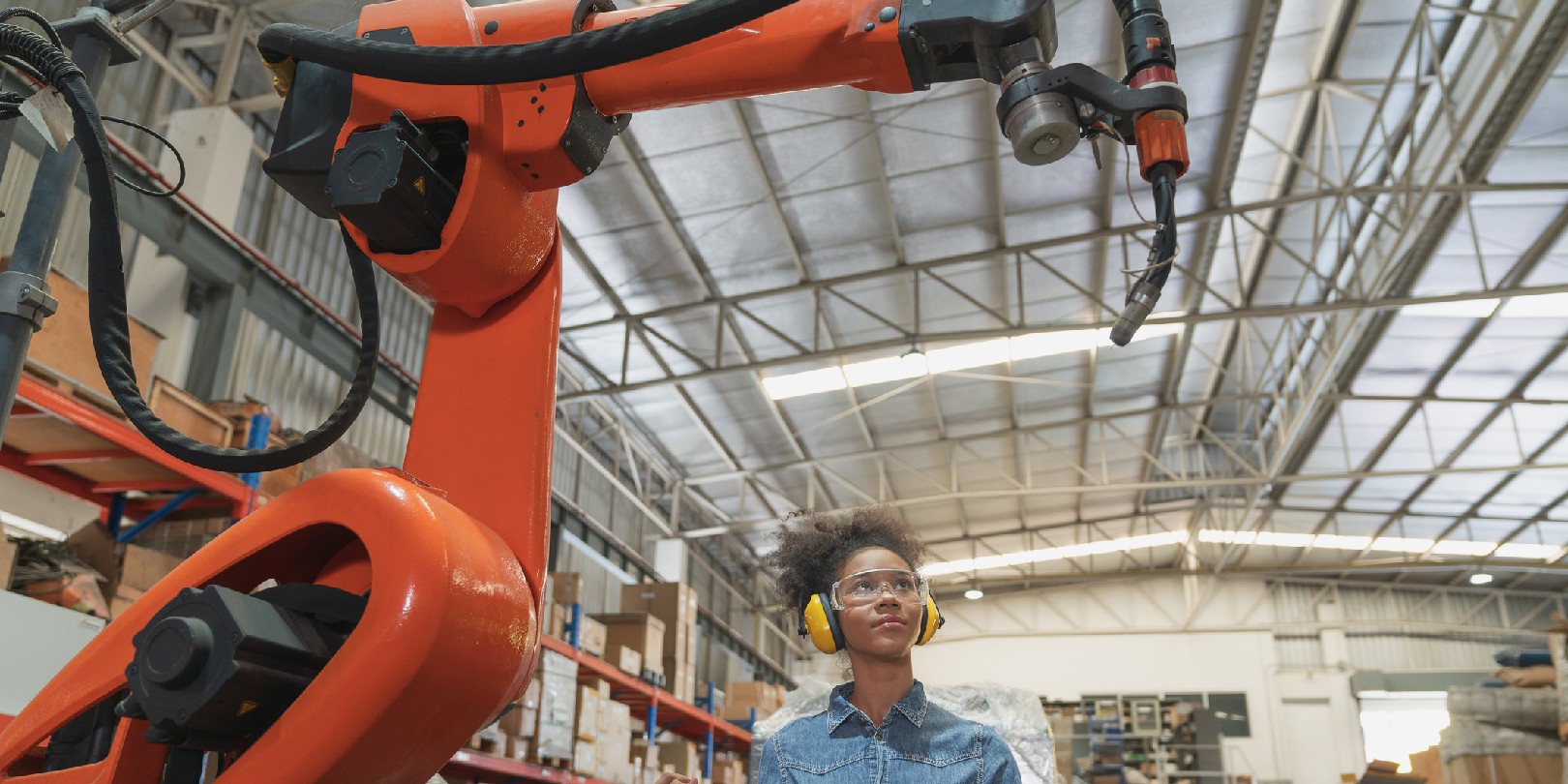Young African American female engineer operating welding robot arm machine in warehouse factory