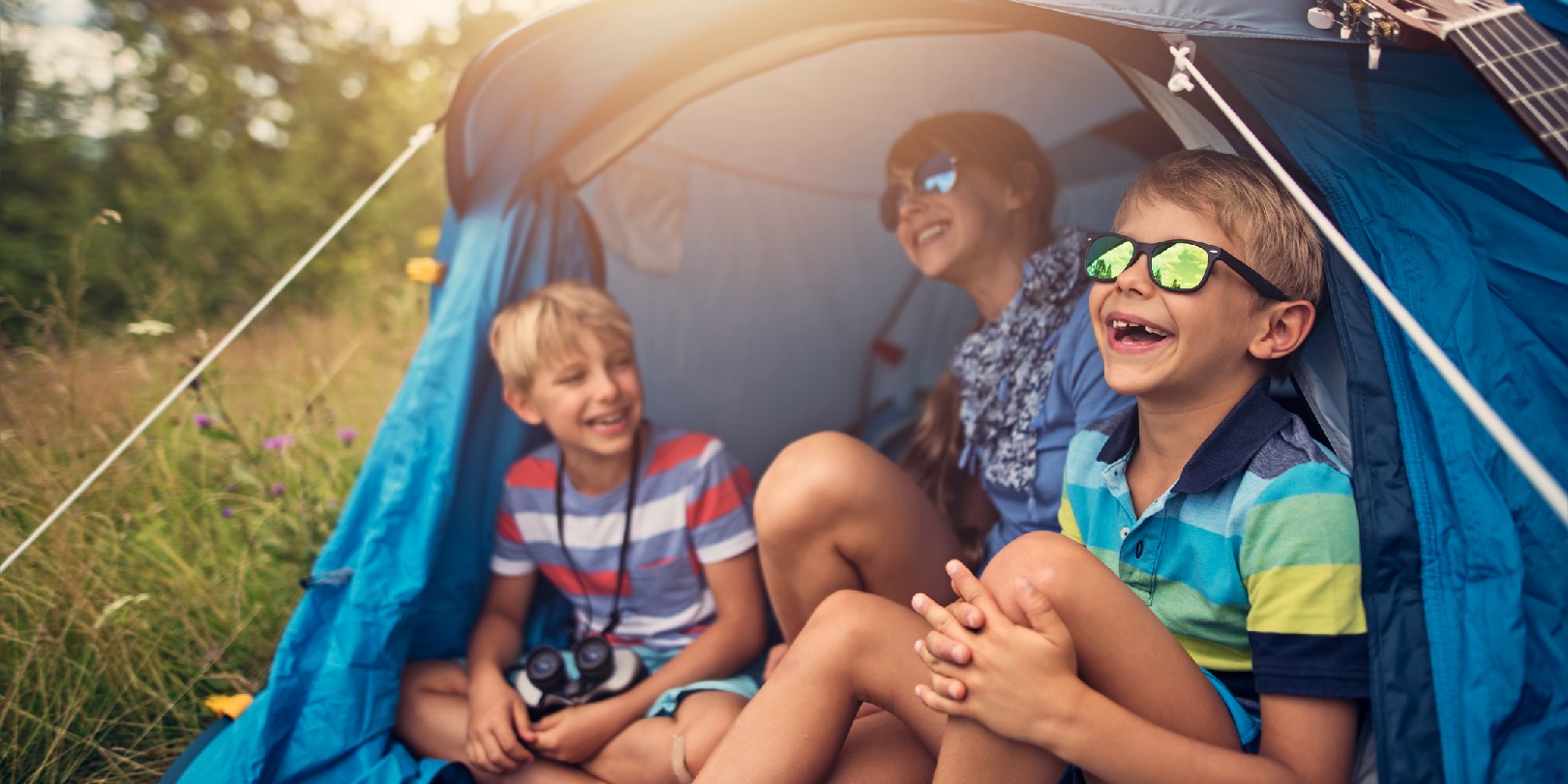 Little girl and her brothers are camping in a blue tent on the forest meadow