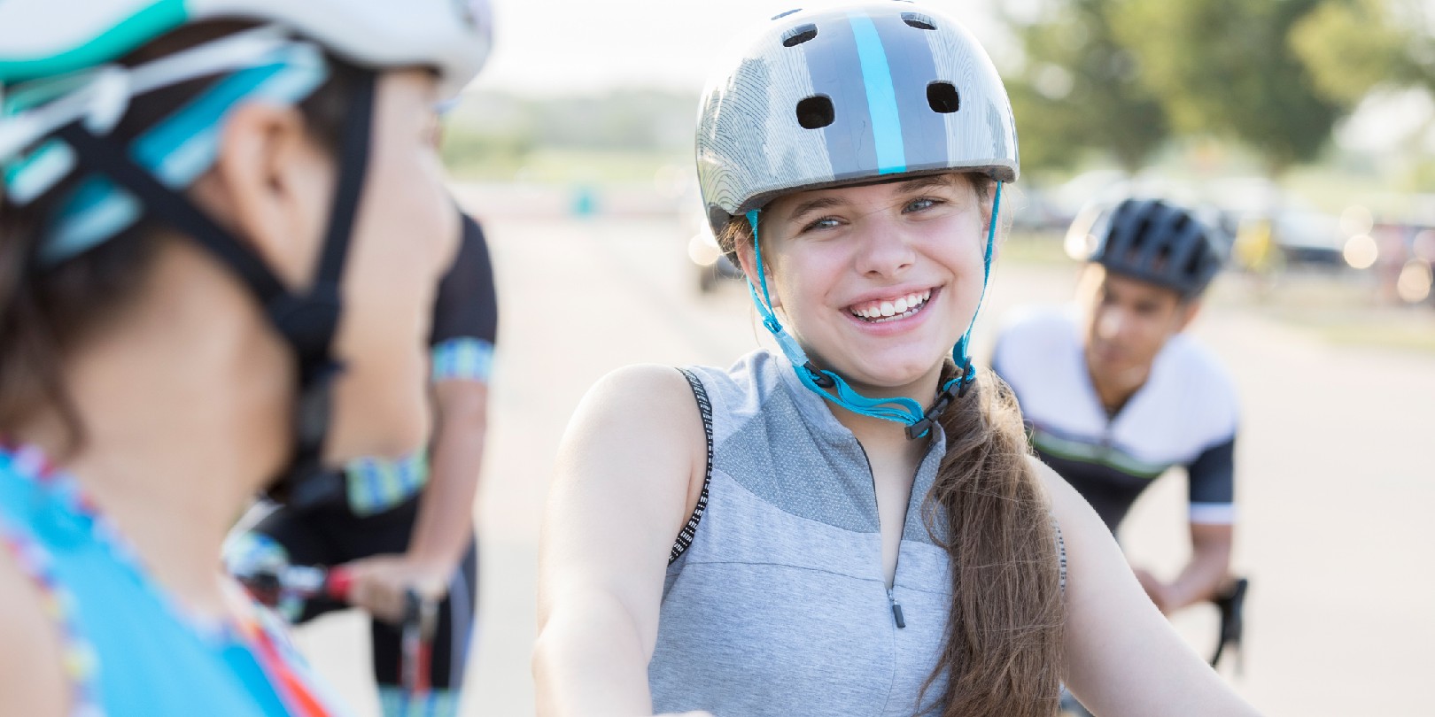 A smiling preteen girl sits on her bike and talks with her unrecognizable mother before a bike race for charity event.