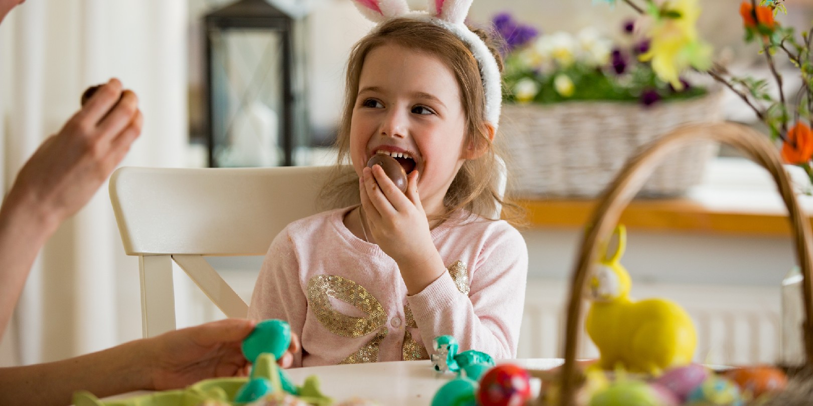 Mother and daughter celebrating Easter, eating chocolate eggs. Happy family holiday. Cute little girl in bunny ears laughing, smiling and having fun.