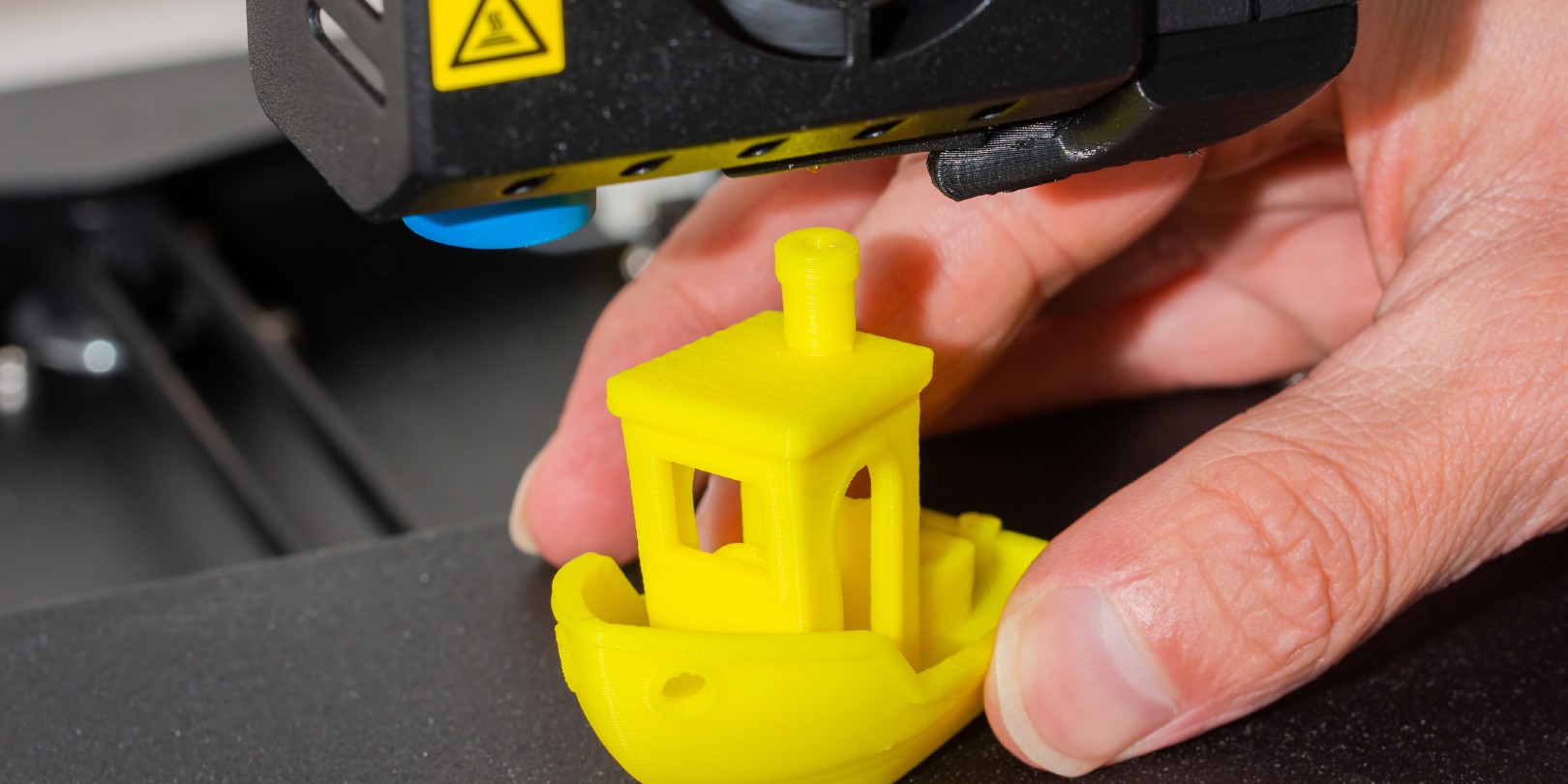Close-up of man hands taking finished 3D printed model of yellow PLA ship