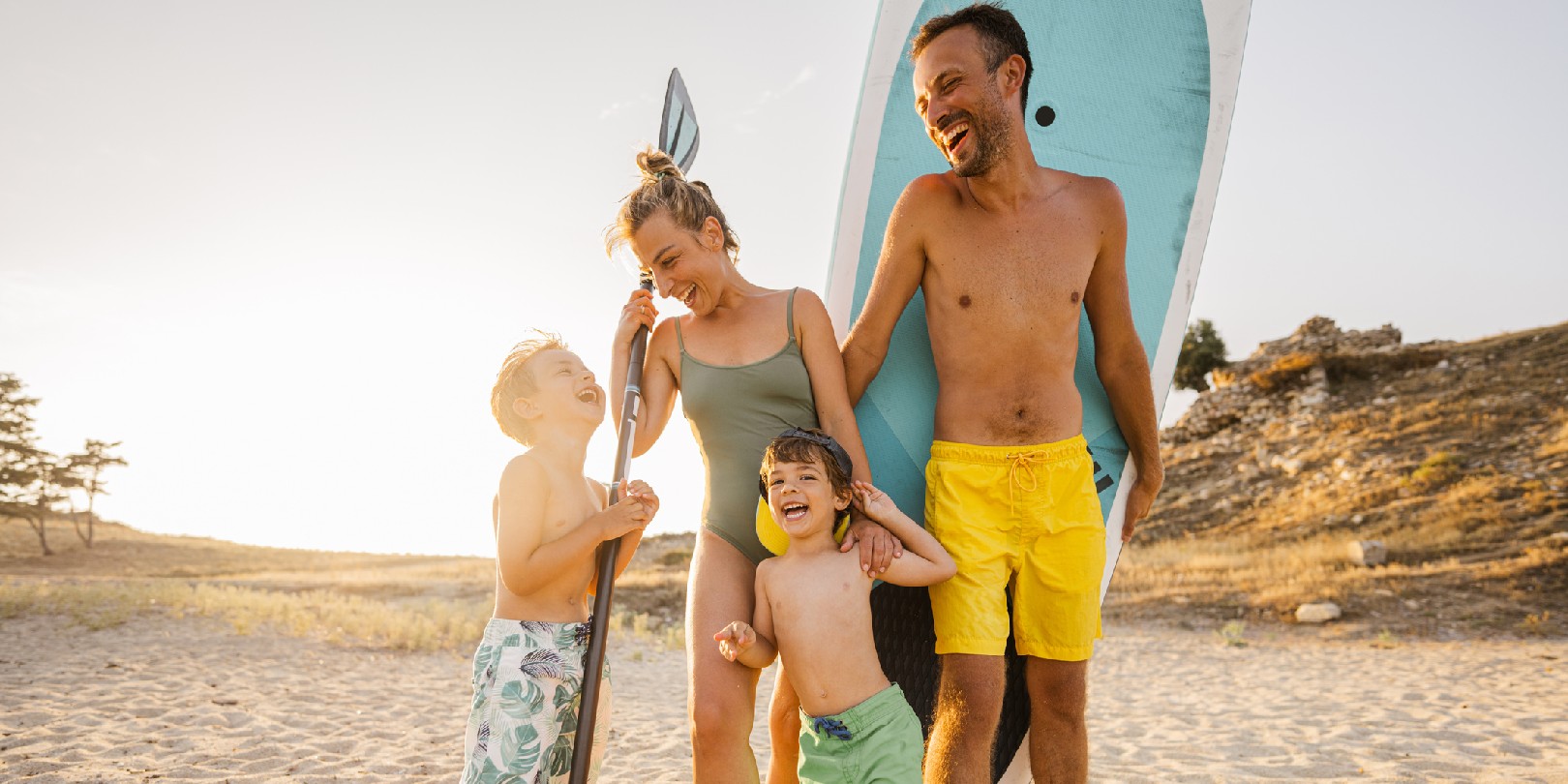 places-to-go-for-holiday the-independence Photo of a smiling family at the beach, ready for paddleboarding