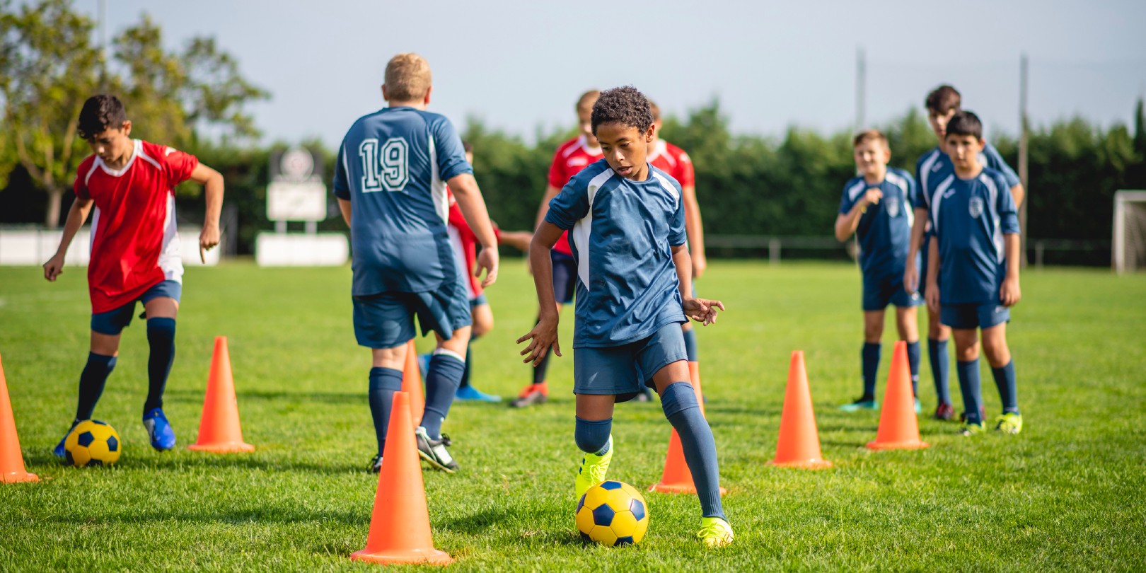 Young male athletes doing dribbling drills around pylons to improve ball control skills.