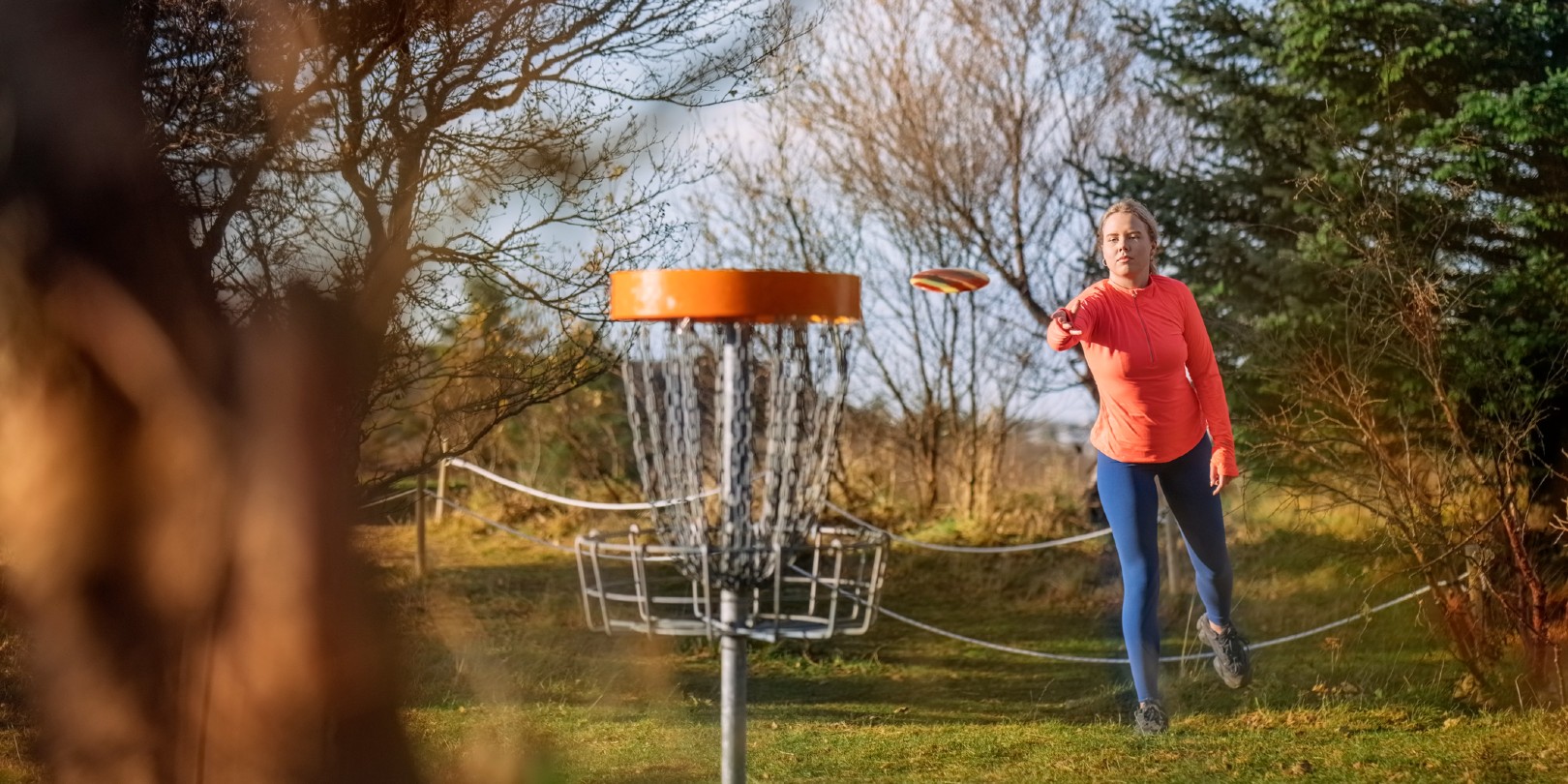 frisbee-golf-for-beginners the-independence Woman tossing a disc into the basket goal. Caucasian woman playing disc golf game outdoors in a park.