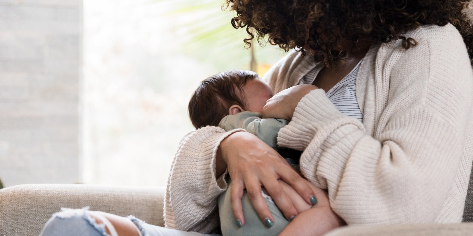 Unrecognizable mom holds baby snugly while breastfeeding