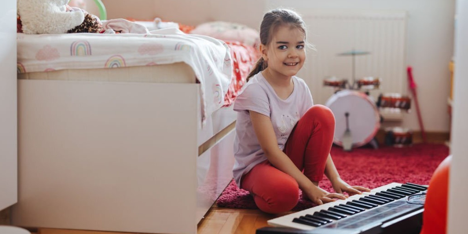 Cute little girl sitting on floor in her playroom and playing synthesizer at home